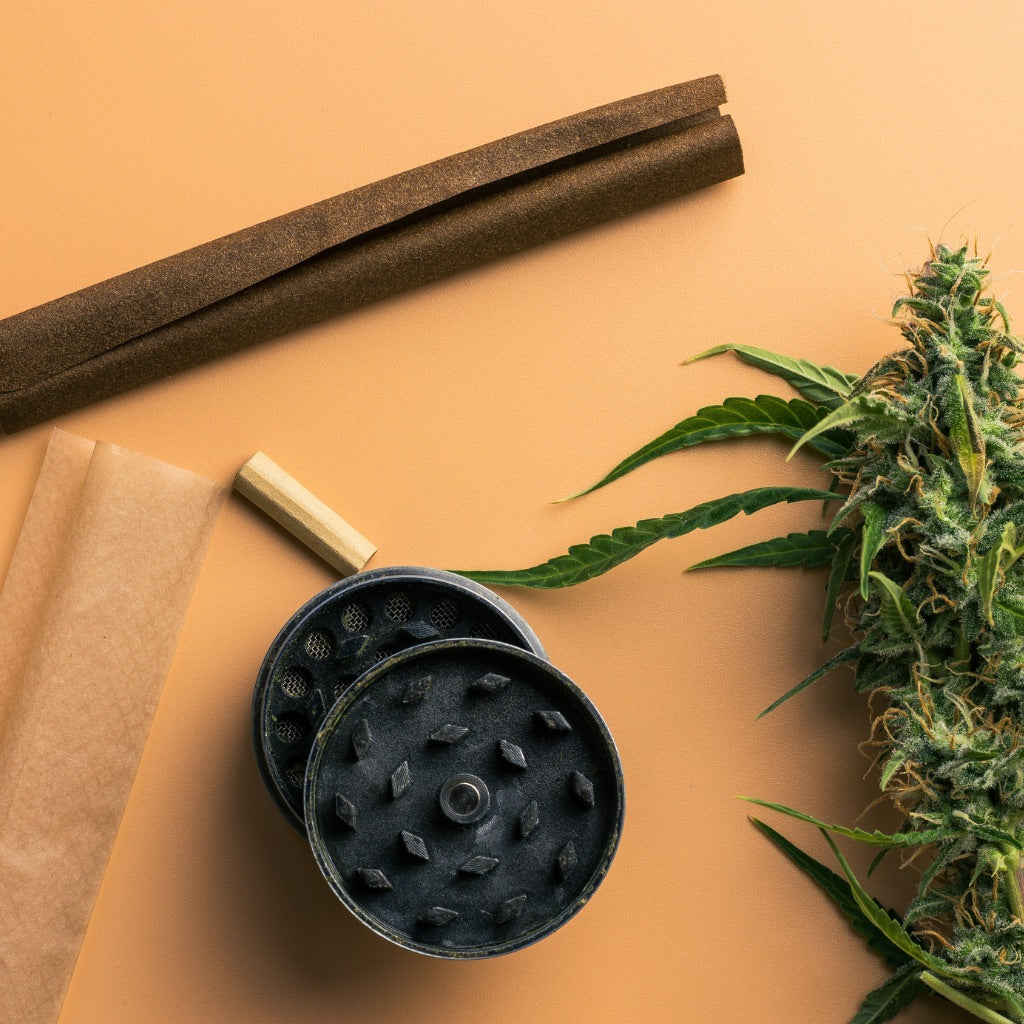 Close-up of cannabis flower, grinder, rolling papers and blunt wrap on beige background. Preparation materials for cannabis consumption.
